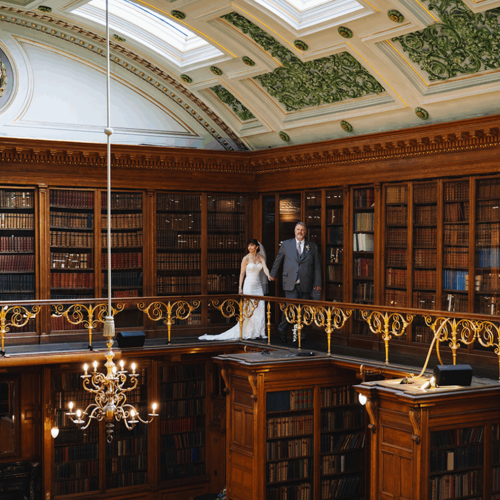 Couple standing on upper balcony inside ornate library.