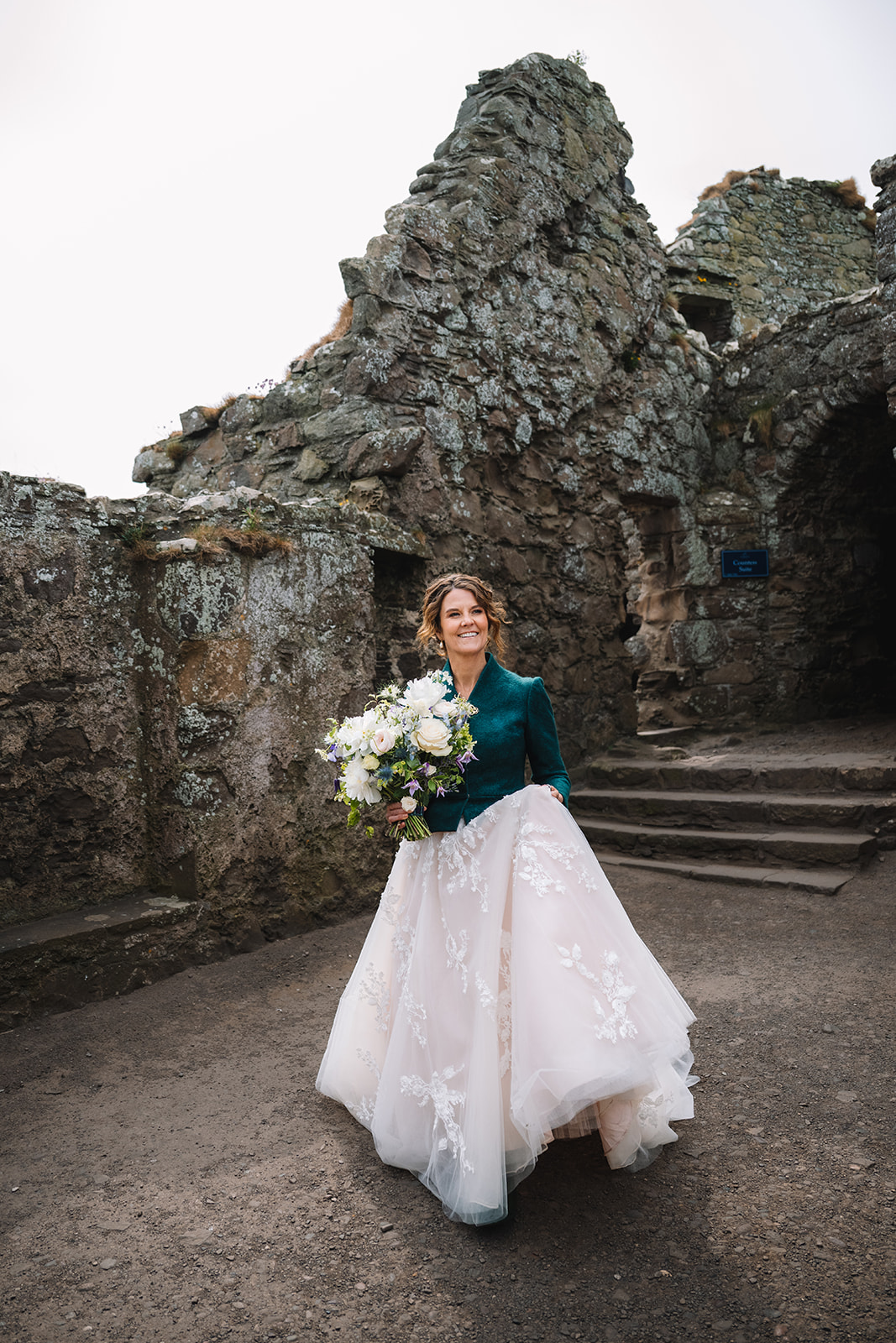 Bride holding bouquet standing near historic stone ruins.