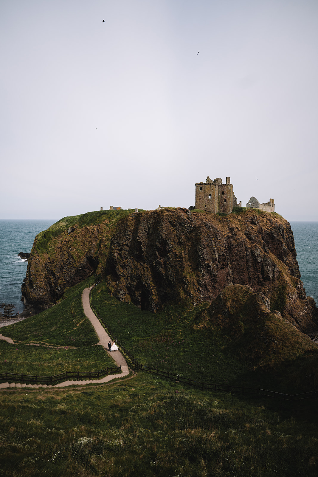 bride and groom walk path leading to Dunnottar Castle