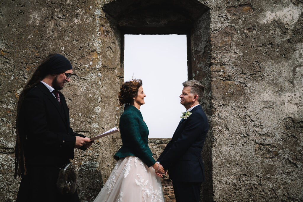 Couple exchanging vows framed in stone ruin doorway.