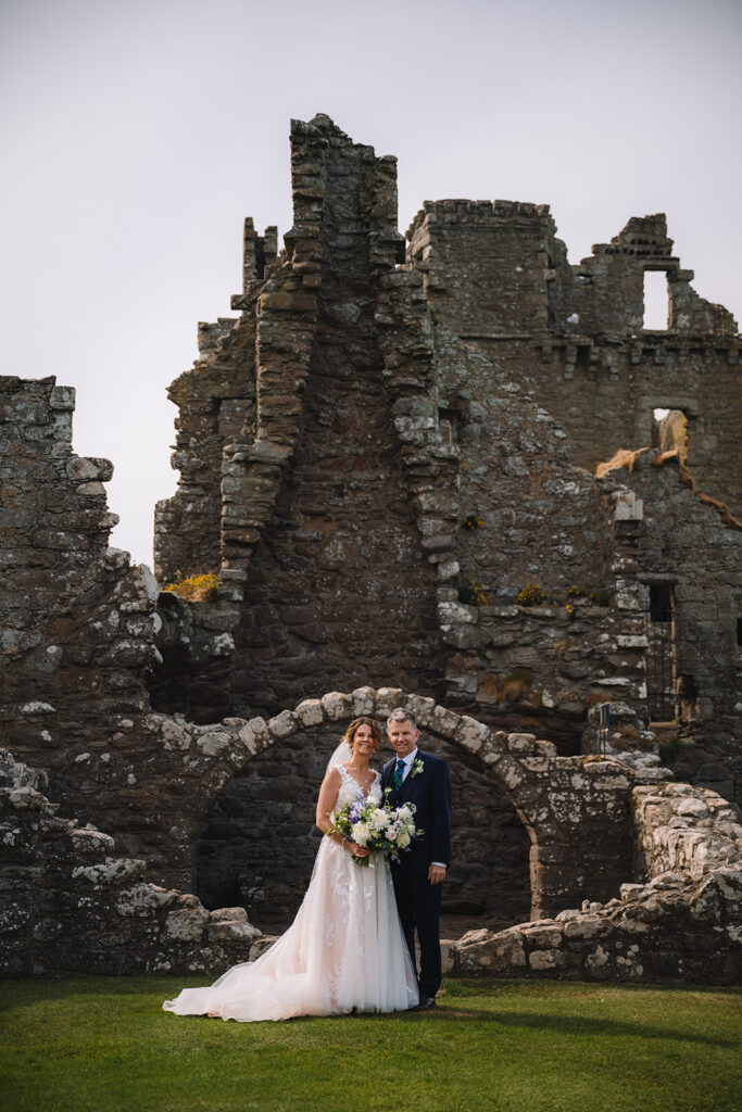 Couple embracing within stone arch of castle ruins.