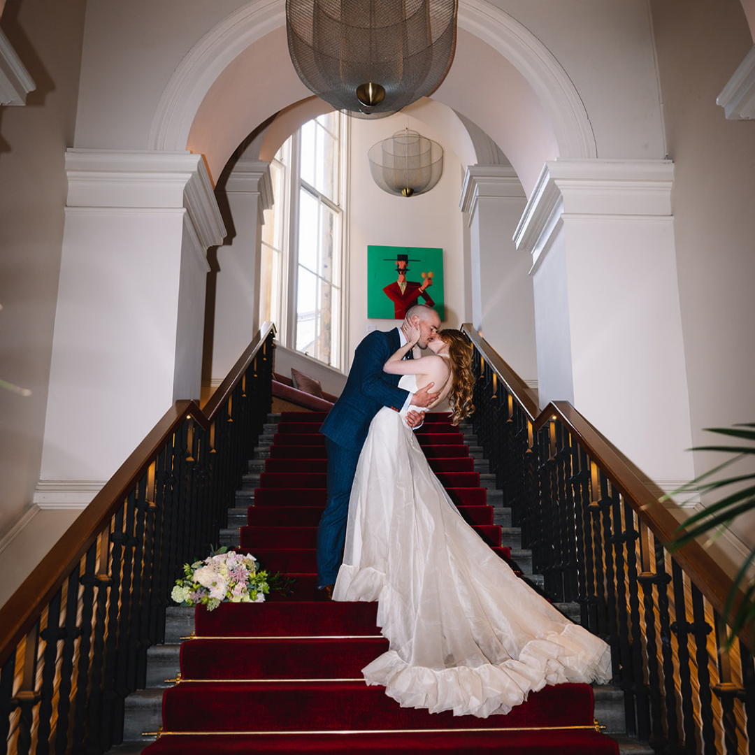 Bride descending staircase in flowing dress with dramatic lighting.