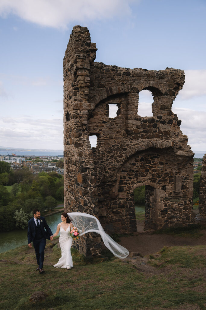 Couple standing beneath tall stone ruin overlooking cityscape.