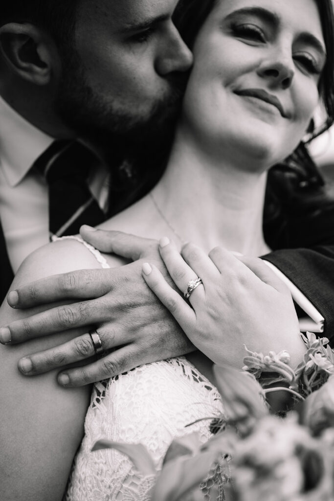 Close-up of bride’s hands with ring as groom embraces her.