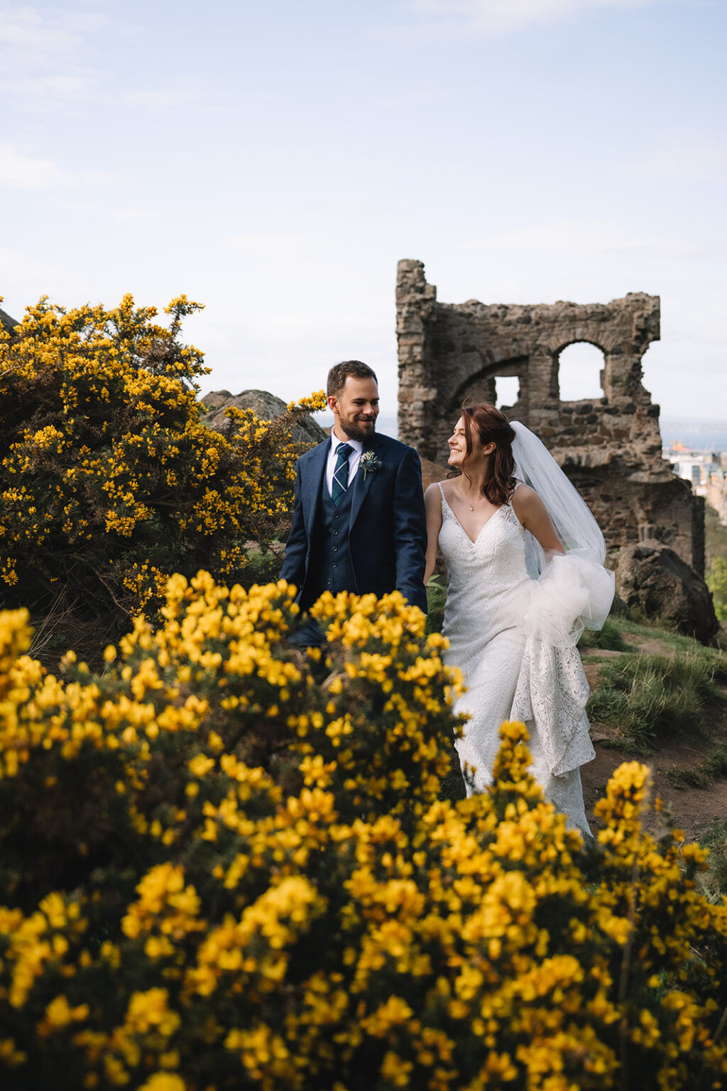 Couple standing among yellow flowering bushes near ruins.