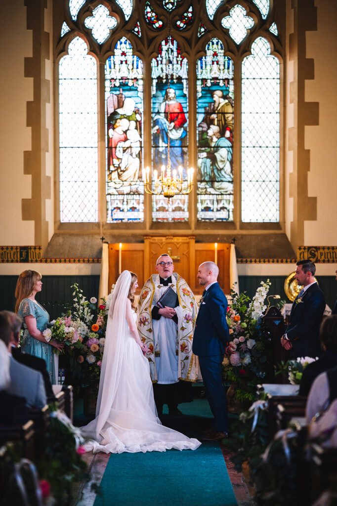 Ceremony inside church with stained glass and floral decor.