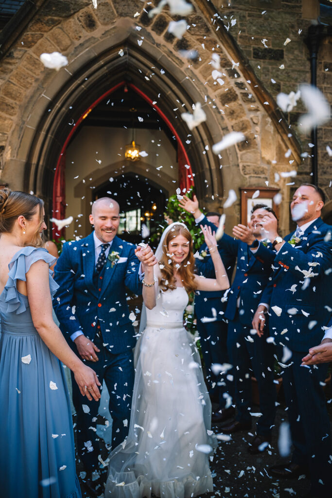 Couple celebrating with confetti surrounded by guests outdoors.