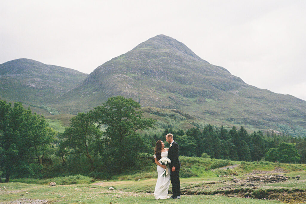 Couple embracing in scenic green valley with mountain backdrop.