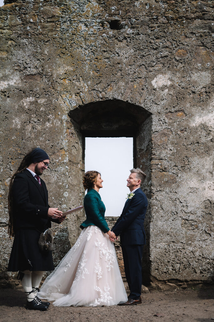 Couple exchanging vows framed within stone ruin doorway by the sea.