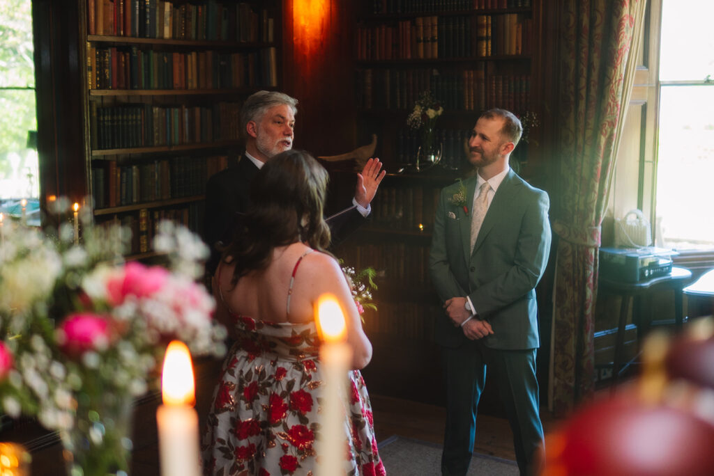 Officiant speaking during ceremony in candlelit library setting.