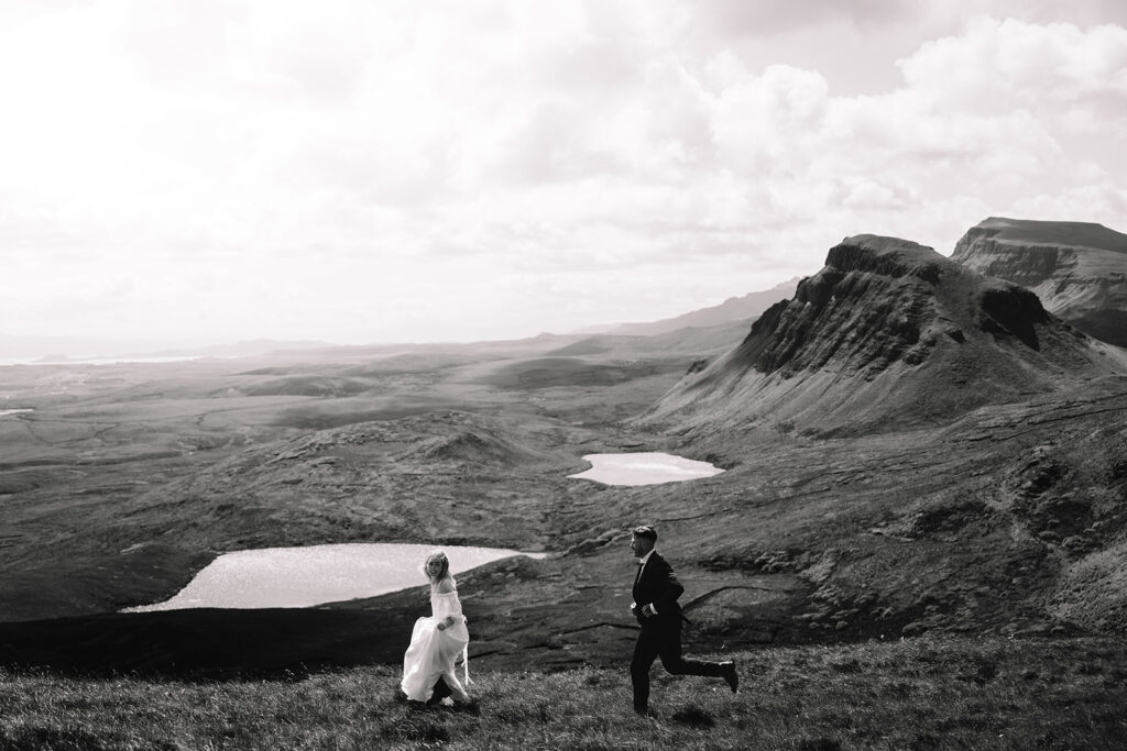 Couple walking through vast valley with lake and hills.
