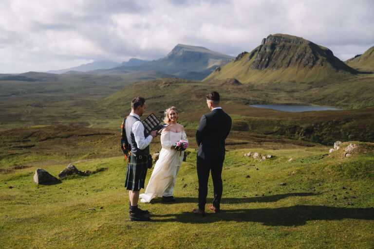 Outdoor ceremony with couple and officiant in scenic setting.