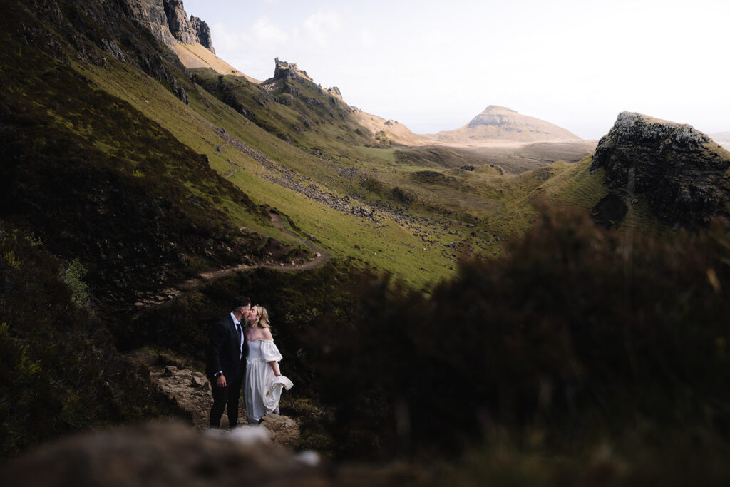 Couple standing together in valley surrounded by towering mountains.
