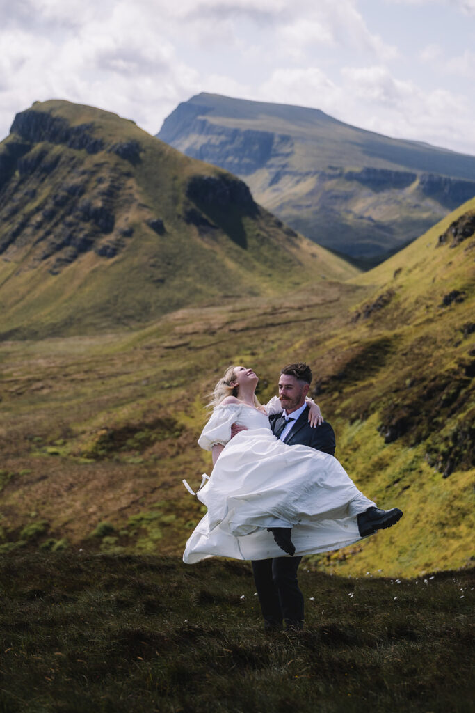 Bride twirling in dress with groom in rugged mountain scenery.