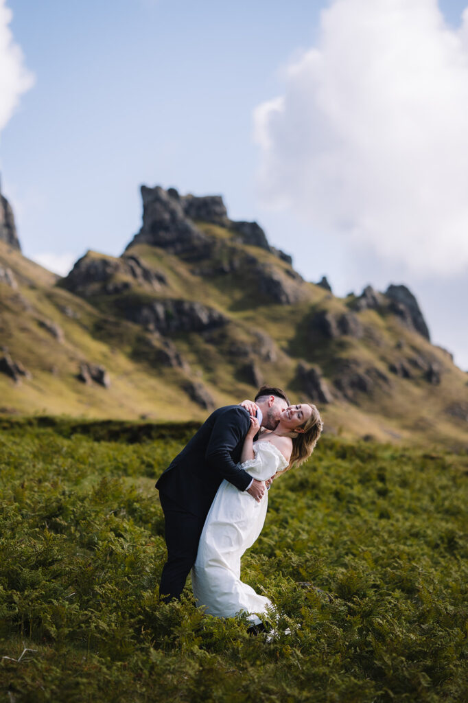 Couple kissing in grassy Highland landscape with rocky peaks.