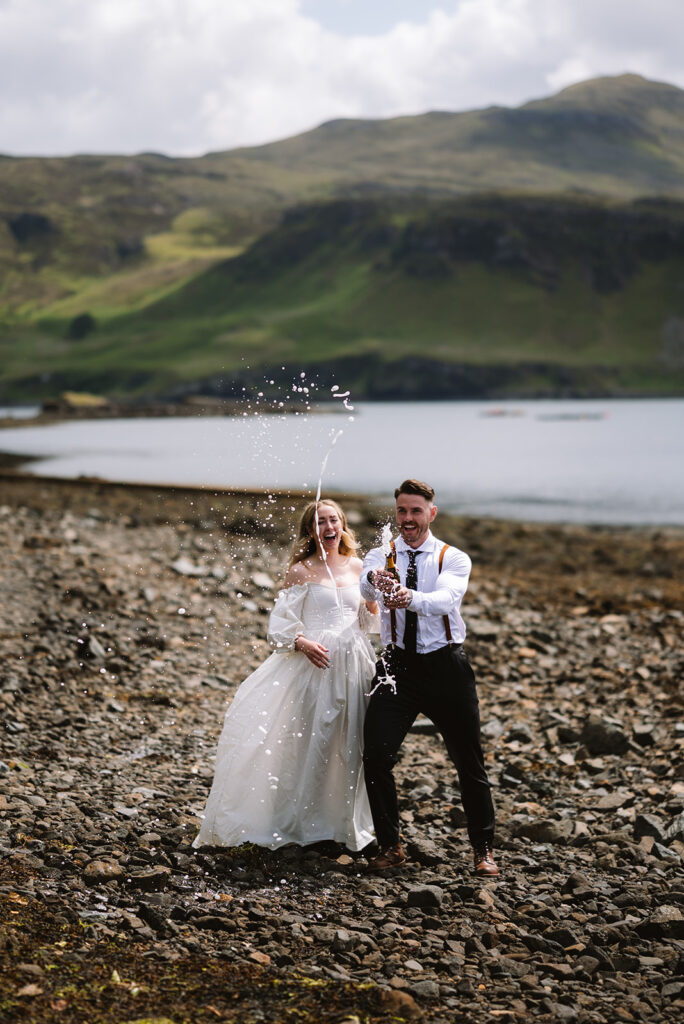 Bride and groom toasting drinks by lakeside.