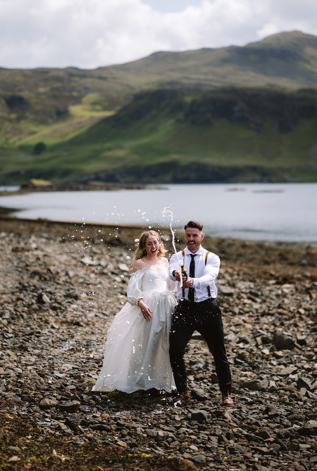Couple celebrating with champagne on rocky beach.