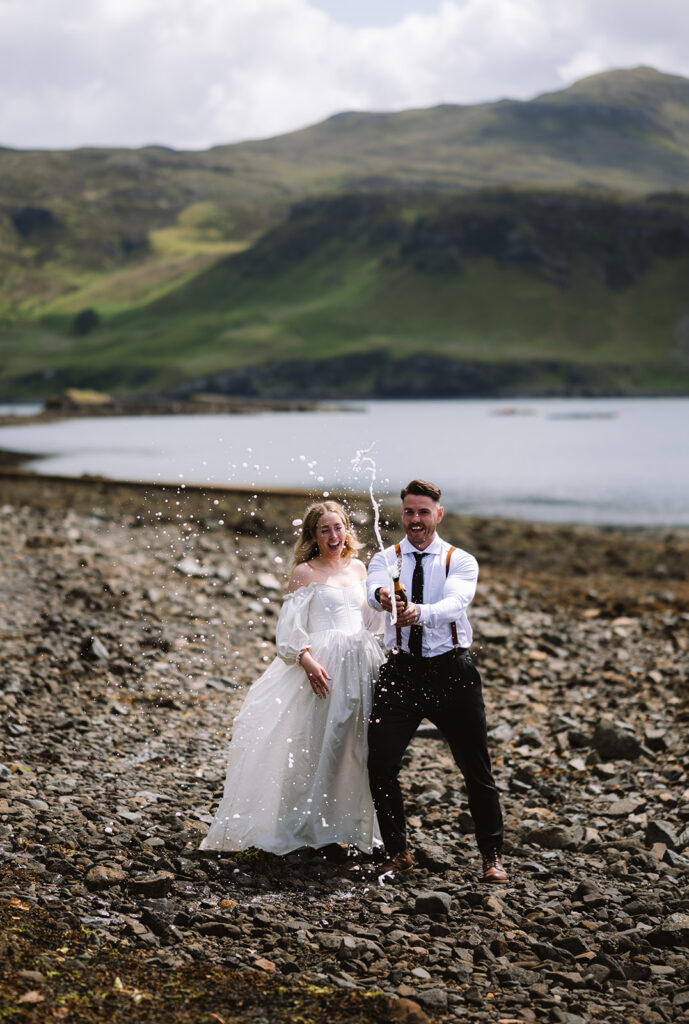 Couple celebrating with champagne on rocky beach.
