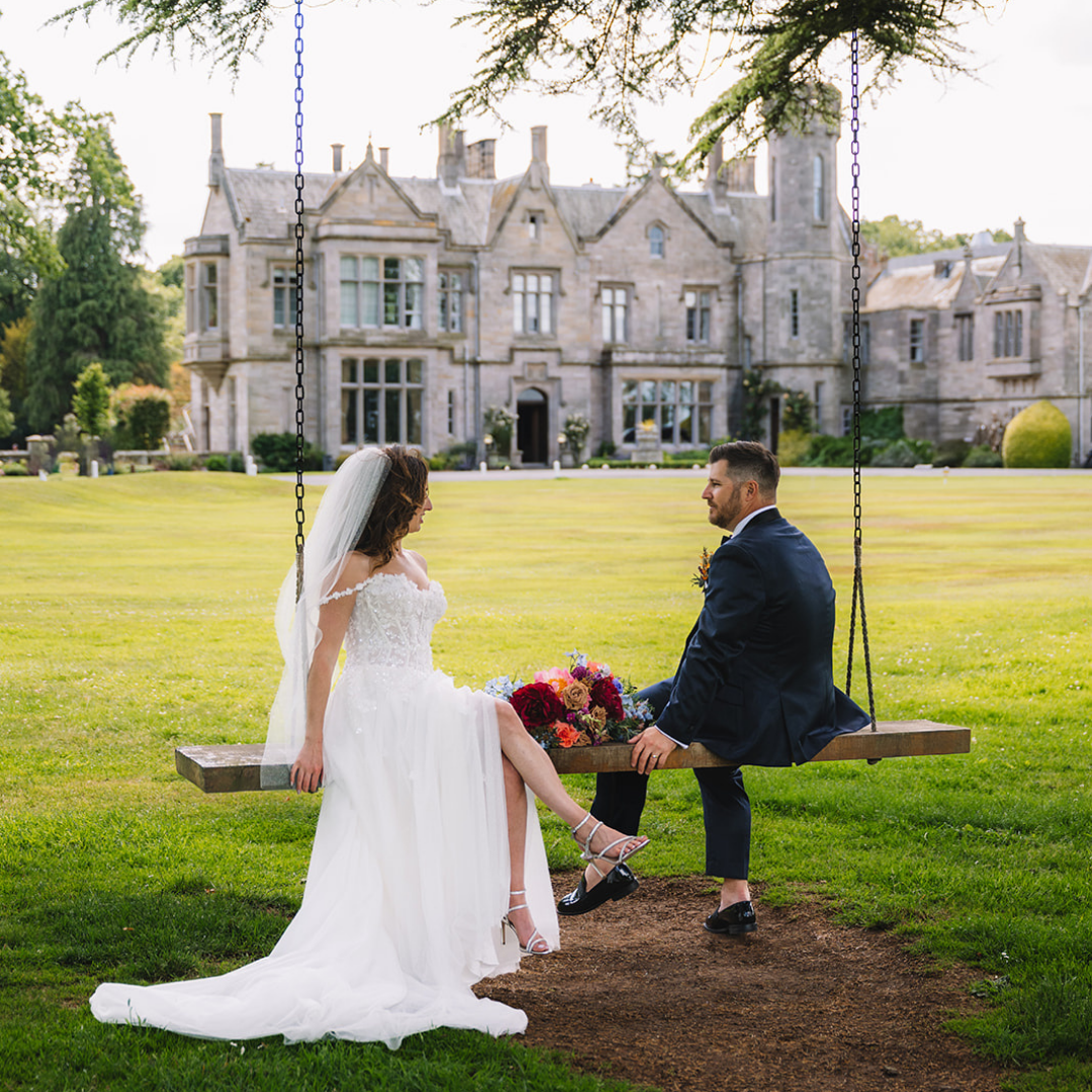Couple sitting together on swing in front of grand estate building.