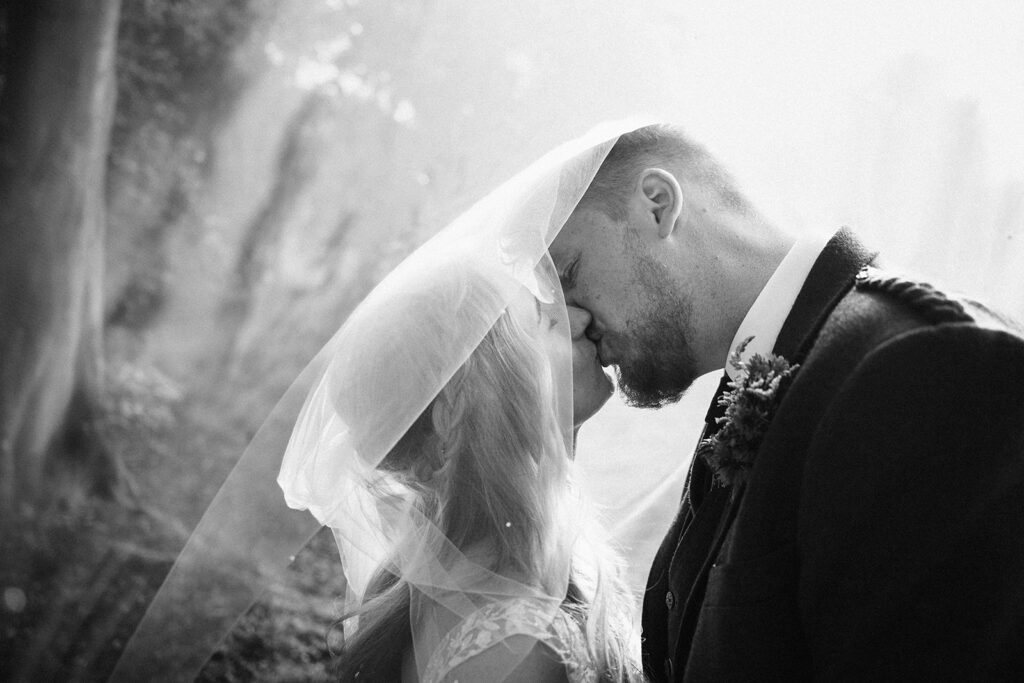 Couple sharing kiss under veil in black and white portrait.