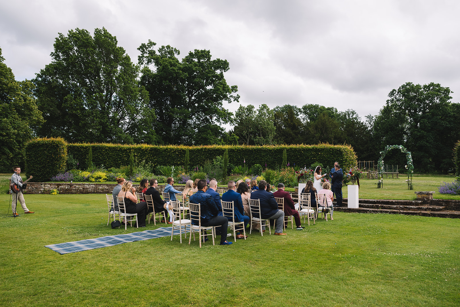 Guests seated during outdoor ceremony on lawn.