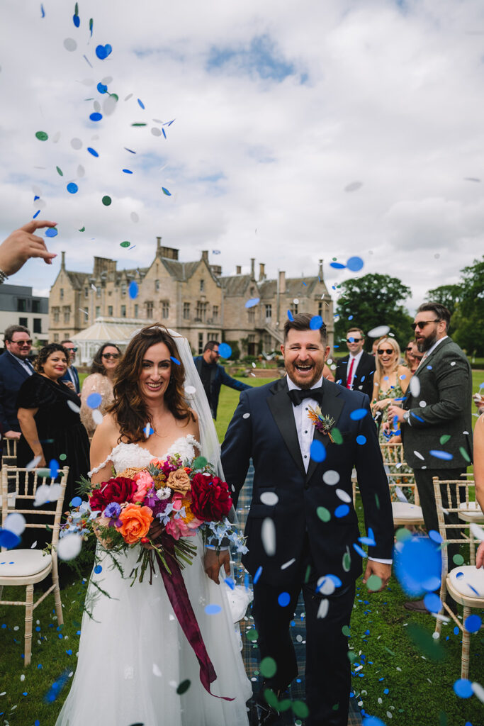 Couple celebrating with confetti outdoors in front of guests.