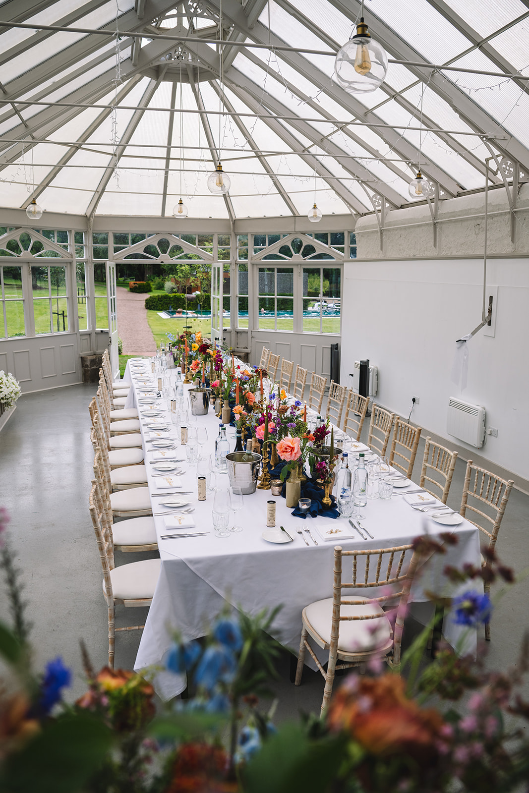 Long banquet table setup inside bright glass conservatory.