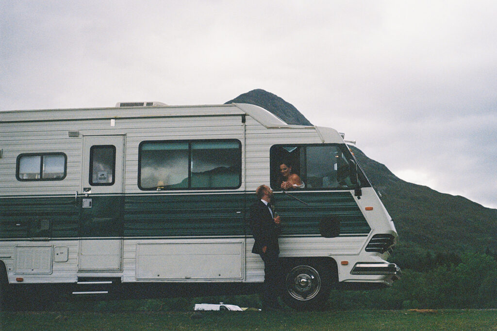 Bride leaning out of vintage camper van window in countryside setting.