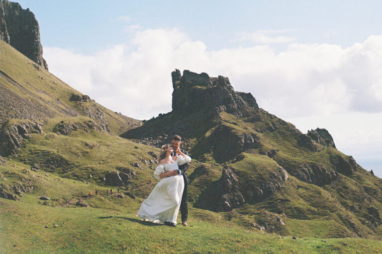 Bride and groom standing near rocky cliff with scenic view.