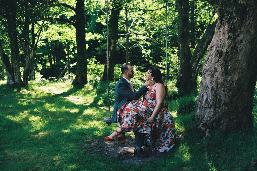 Couple sitting together beneath tree in sunlit forest.