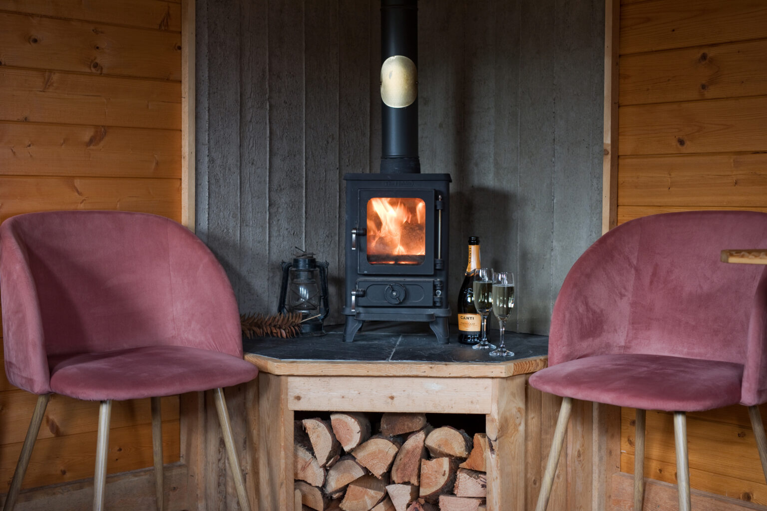 Wood-burning stove with stacked logs in cozy cabin setting.