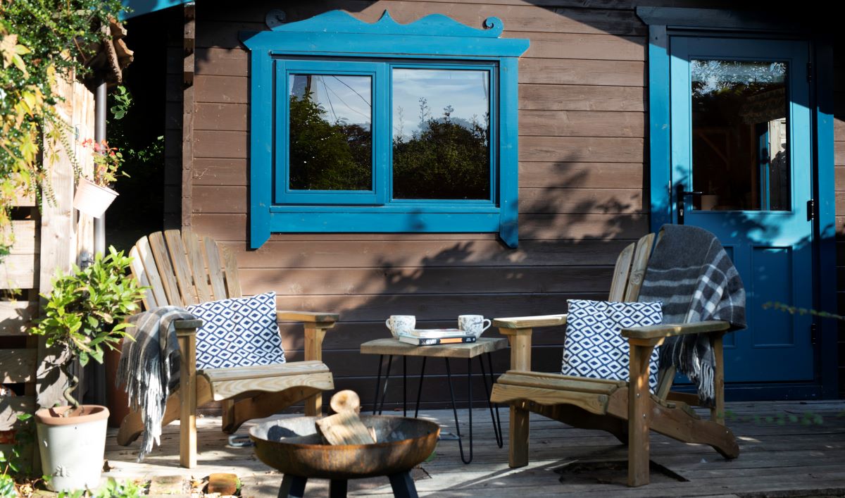 Cozy outdoor seating area beside cabin with blue window.