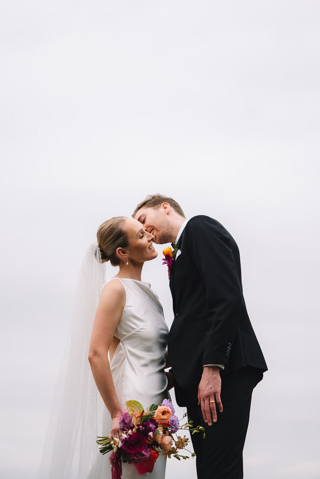 Bride and groom sharing kiss against soft neutral background.