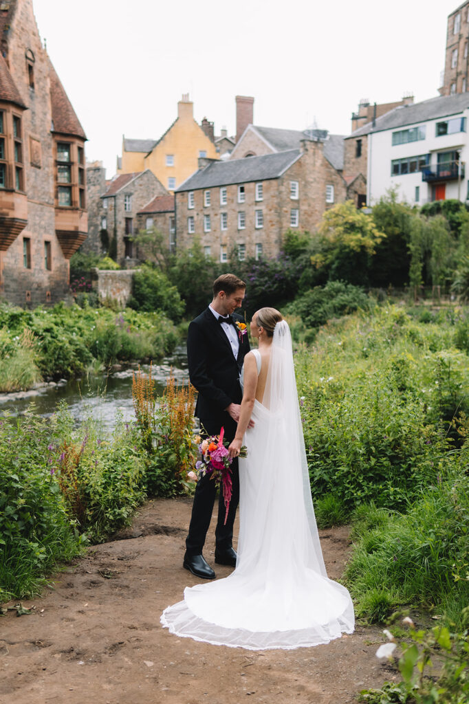 Couple standing by riverside with colorful houses in background.
