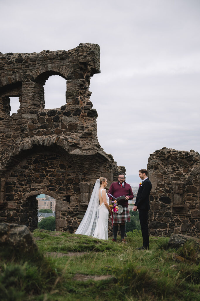Couple standing with officiant during ceremony at historic ruins.