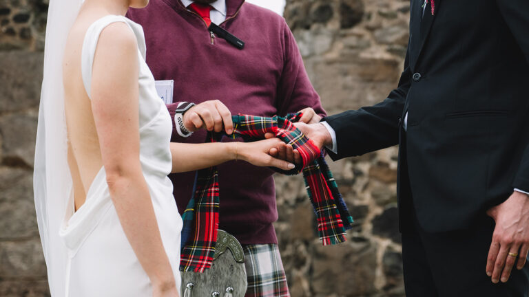 Handfasting ceremony with tartan ribbon wrapped around hands.