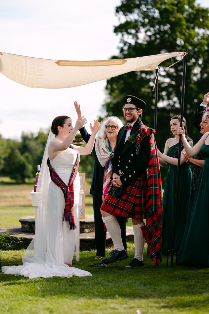 Couple celebrating during outdoor ceremony with raised hands.