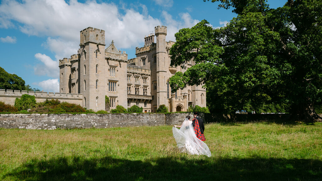 Couple standing in front of castle venue on green lawn.
