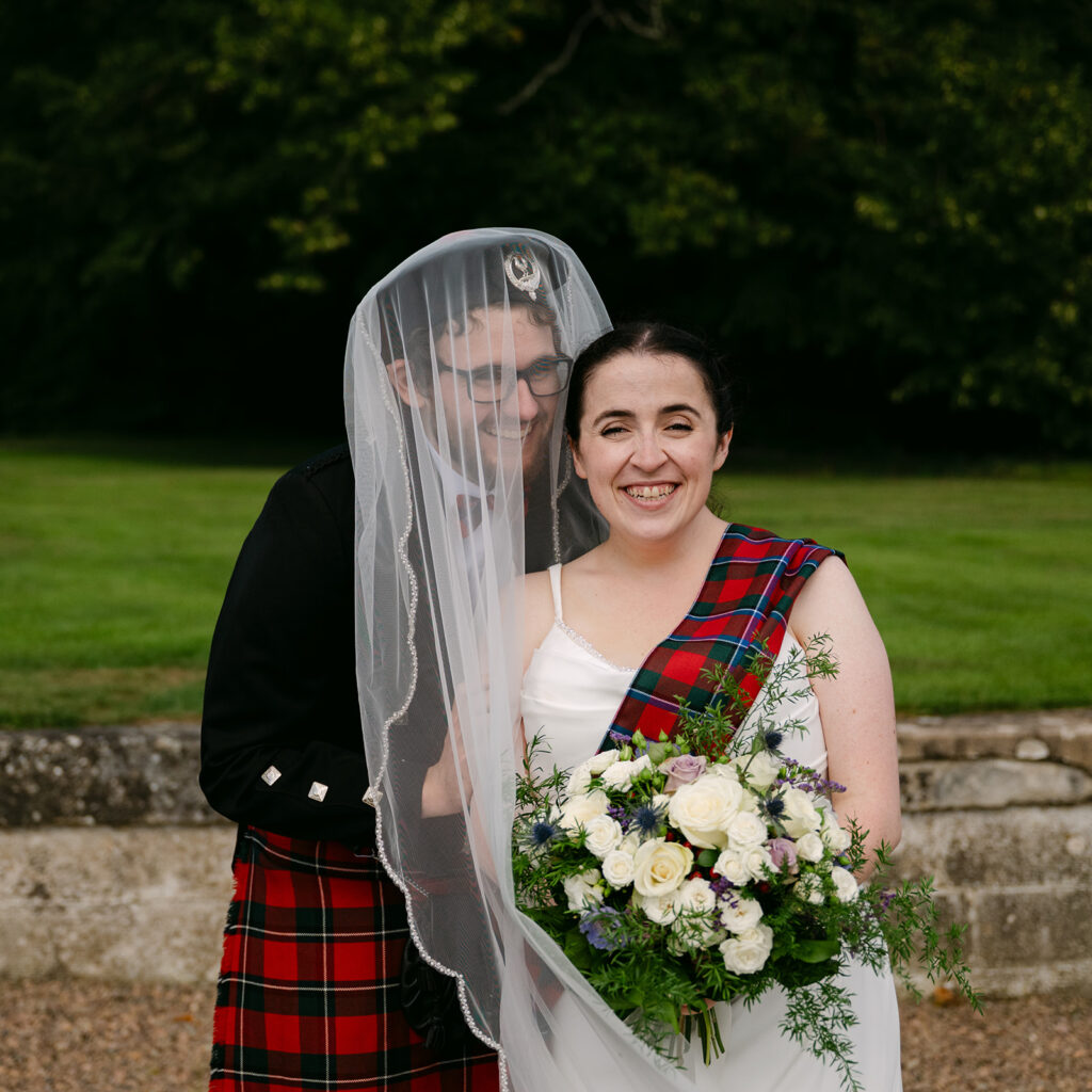 Bride and groom smiling together with veil and bouquet.