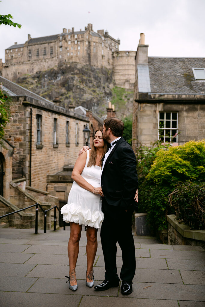 Couple standing together on cobbled street near historic buildings.
