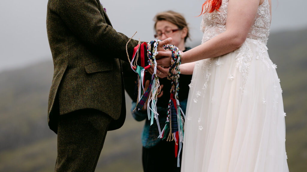 Couple holding hands during handfasting ceremony with ribbons.