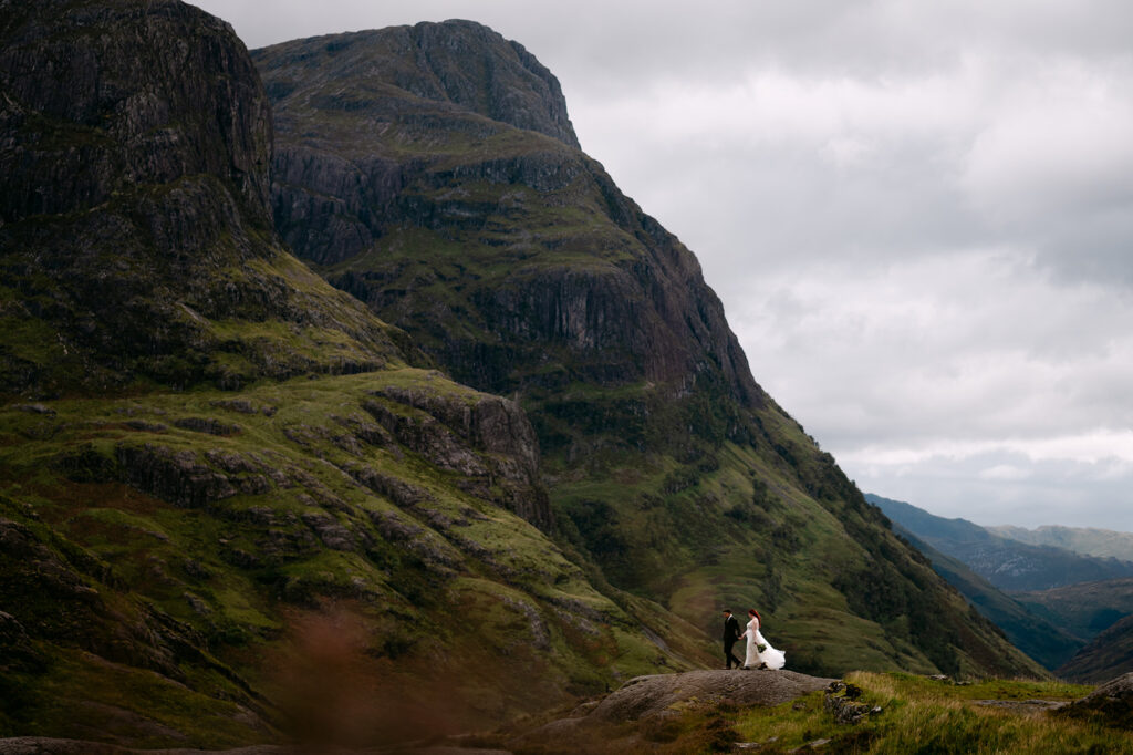 Couple standing in distance within dramatic mountain scenery.