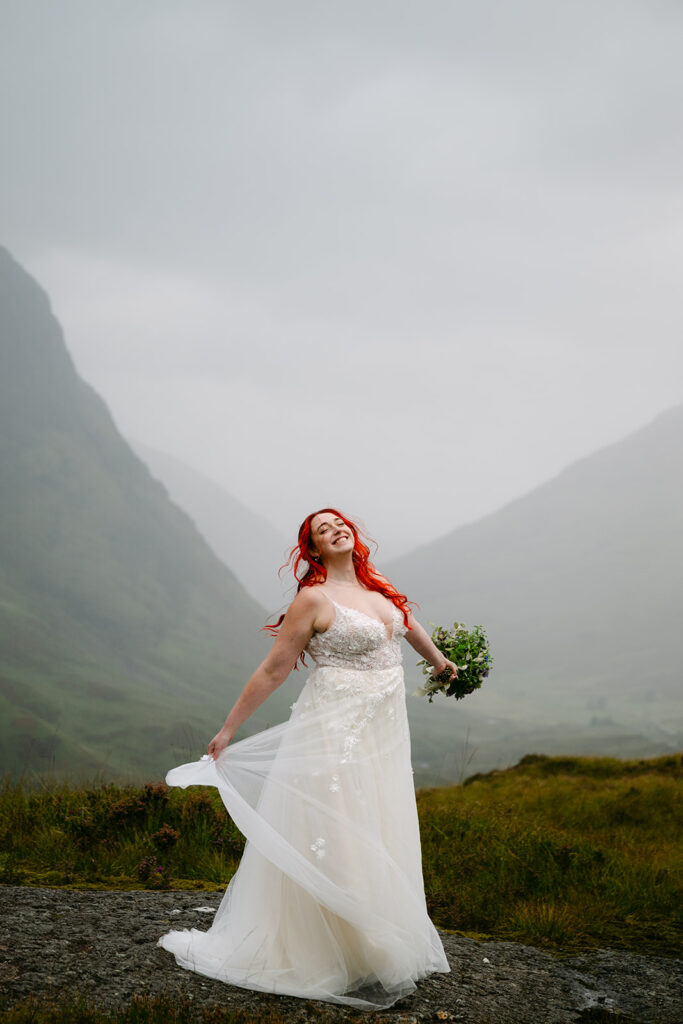 Bride walking joyfully through mountain valley holding bouquet.