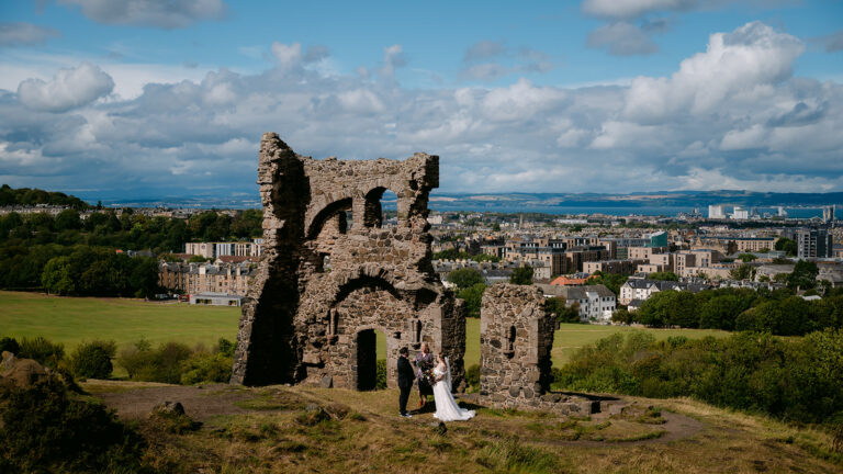Couple standing by historic ruins overlooking city skyline.