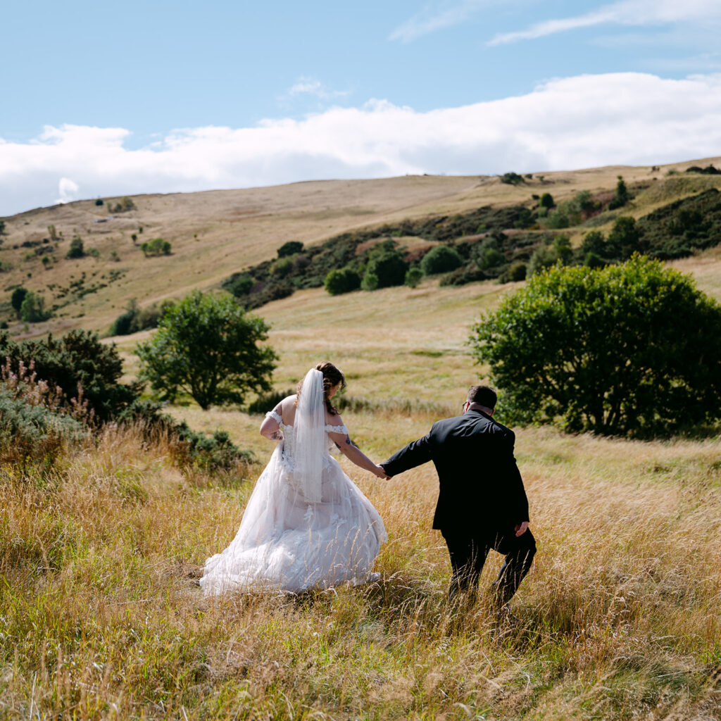 Couple running together through grassy field in sunshine.