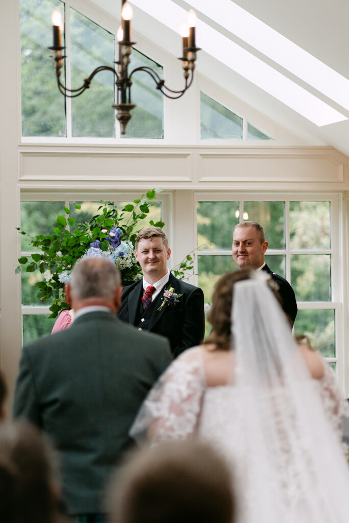Bride walking down aisle toward groom in bright indoor venue.