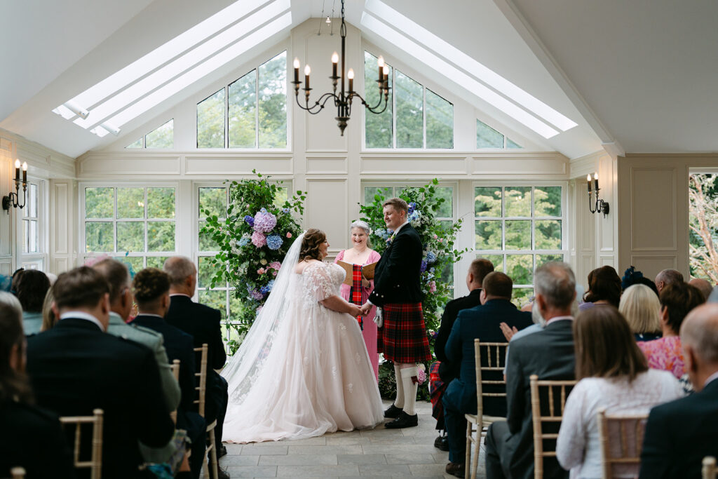Wedding ceremony taking place in light-filled room with guests.