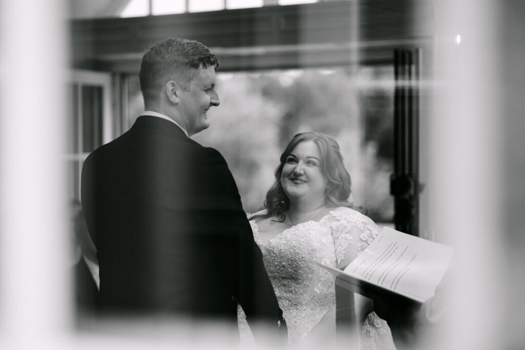 Couple smiling together during ceremony in black and white.