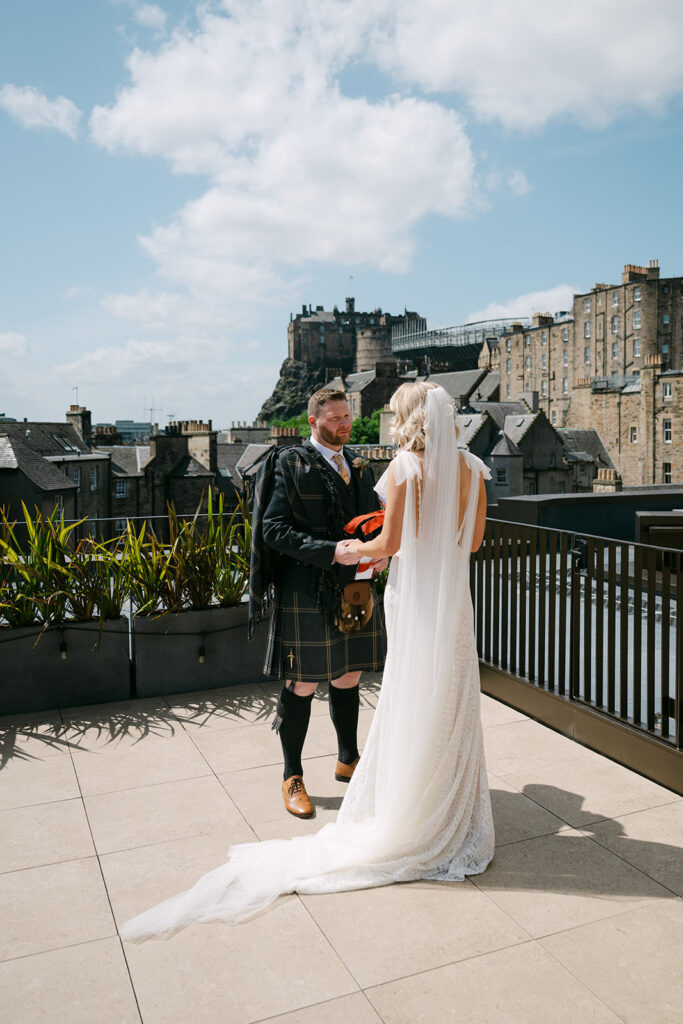 Bride and groom on rooftop terrace with city backdrop.
