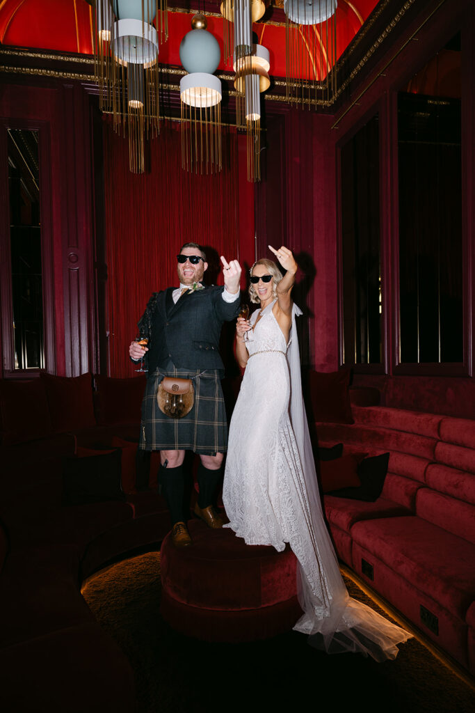 Couple posing playfully in reception space with red backdrop.